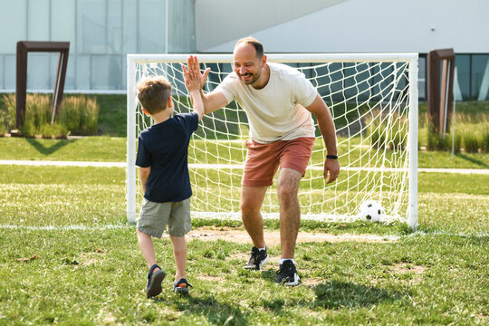 man with child playing football outside on field