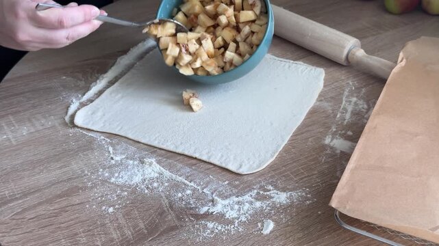 Adding diced apple filling from bowl onto puff pastry for homemade apple strudel