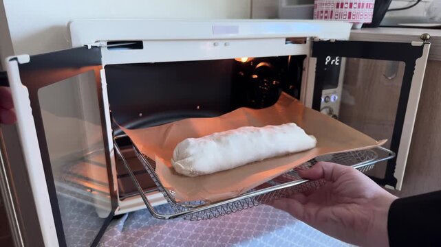 Placing homemade apple strudel into oven for baking on parchment paper