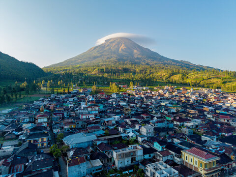 Aerial view of the Tambi village nestled at the foot of Mount Sindoro with lush green slopes, colorful rooftops, and morning sunlight in Kejajar, Central Java, Indonesia.