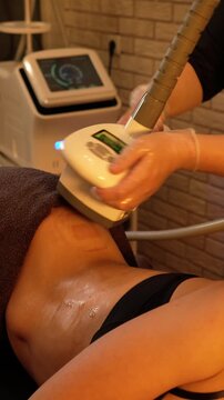 Vacuum roller massage. Anti-cellulite stage. Dim atmospheric warm light. Masseuse massages woman's sides with a device. self-care, care, weight loss