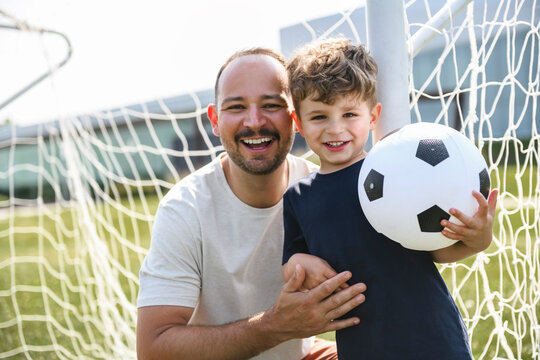 man with child playing football outside on field