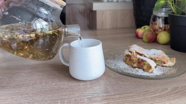 Pouring herbal tea into a mug beside freshly baked homemade apple strudel