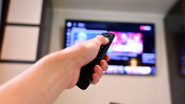 Hand holding black remote control pointed at television screen