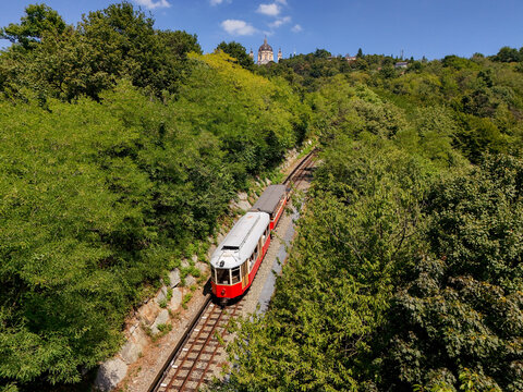 Aerial view of the historic red Sassi-Superga rack railway train climbing through the lush green forest towards the Basilica of Superga in Turin, Piedmont, Italy.