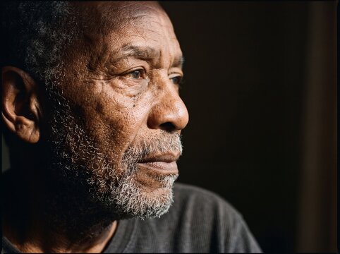 Close Up Portrait of a Thoughtful Senior African American Man with Wrinkles and Gray Beard Looking Away Against Dark Background