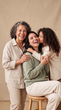 A happy family portrait of a grandmother, mother, and daughter laughing together and sharing affection in a bright studio setting