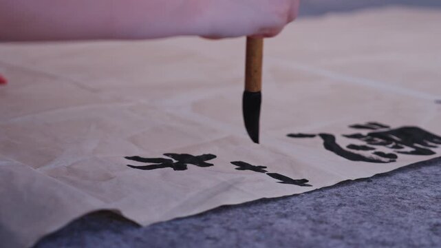 Hand holding a brush to complete black Chinese characters on brown rice paper