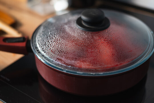 A pot sits on a kitchen stove with vapor forming under the lid as food cooks inside.