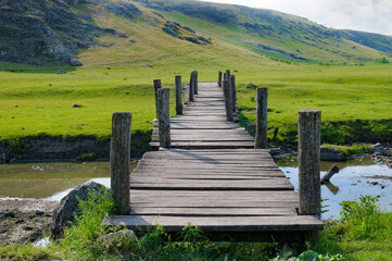 Obraz premium Old Wooden Footbridge Over a Stream in a Scenic Mountain Valley Landscape During Summer Day
