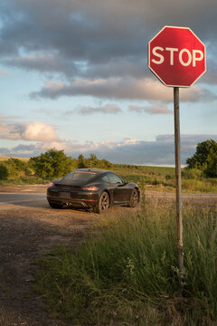 dark Porsche Cayman, Porsche 718, with streamlined shape, roadside road sign stop, sunset light