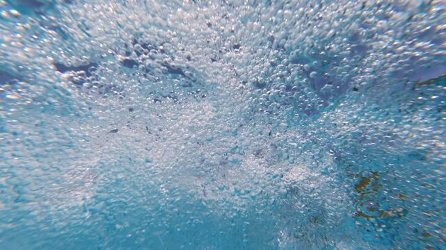 Underwater low-angle footage showing air bubbles rising through clear swimming pool water from a circulation return jet. The moving bubbles create an abstract and dynamic aquatic background.