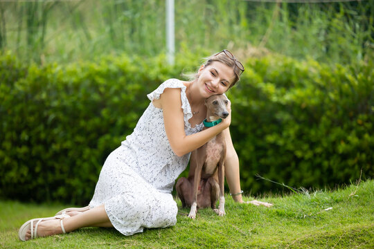 young caucasian woman embraces her gray Italian Greyhound dog, appearing relaxed and content. Home pets. woman holding and hugging her cute dog while walking in the park Outdoor
