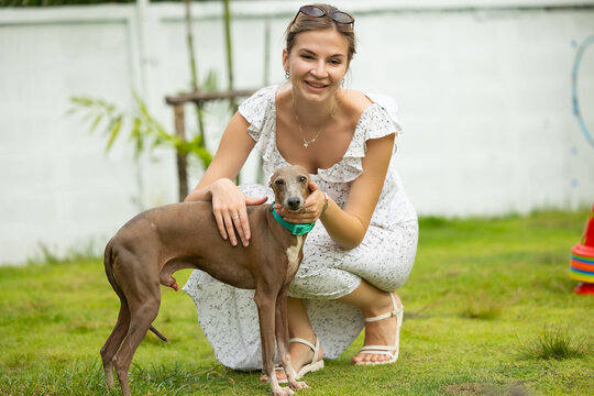 young caucasian woman embraces her gray Italian Greyhound dog, appearing relaxed and content. Home pets. woman holding and hugging her cute dog while walking in the park Outdoor
