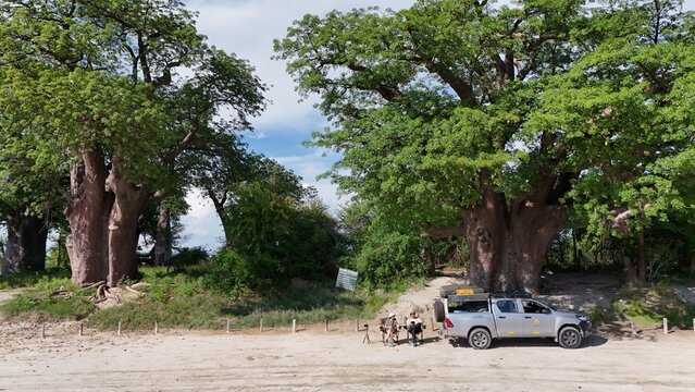 Aerial view of the Khama Rhino Sanctuary featuring large baobab trees, a safari pickup truck parked nearby, and two people sitting in chairs in Paje, Central District, Botswana.