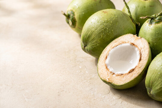 Fresh young green coconuts with opened coconut on cream stone background and copy space