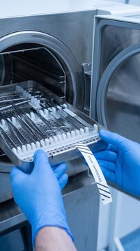 Sterile medical instruments in autoclave with gloved hands handling tray