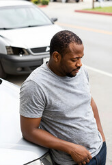 Fototapeta premium African american man leaning on a damaged car after an accident, insurance claim and vehicle repair