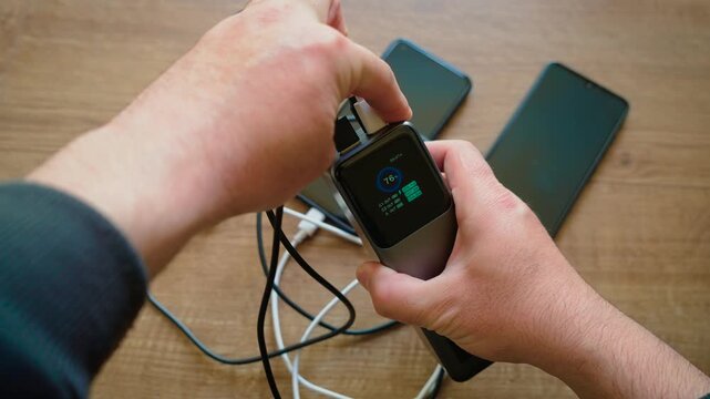 Unplugging smartphone cables from power bank stopping charging for connected devices. Removing connectors from external battery while charge indicator remaining visible on screen. Ending power supply