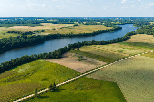 Aerial view of the winding river flowing through lush green agricultural fields and meadows near the town of Juzintai, Panevezys County, Lithuania.