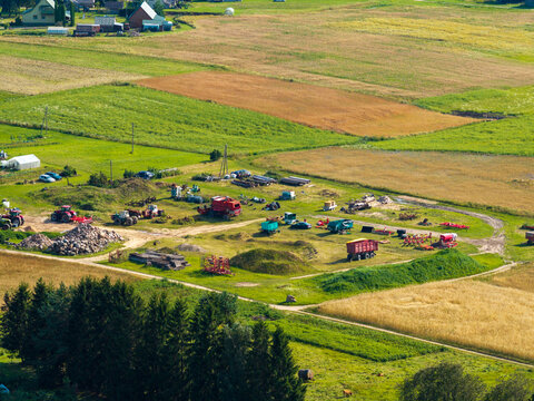 Aerial view of agricultural fields and farm machinery including tractors and trailers in the rural landscape of Juzintai, Panevezys County, Lithuania.