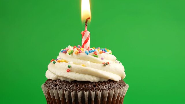 Single chocolate cupcake with vanilla frosting and a flickering candle flame rotating slowly against a chroma key green background