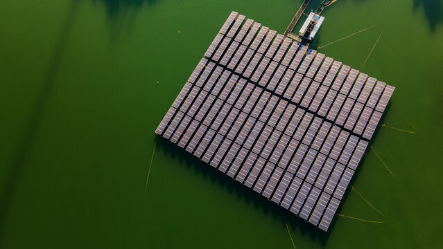 Top down aerial view of floating solar panel array generating clean renewable energy on deep green water surface reservoir
