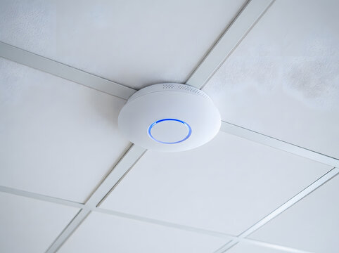 Modern wireless access point mounted on ceiling | Wi-Fi router with blue LED light for office | Network connectivity device on commercial ceiling tile | Smart home security sensor with glowing ring