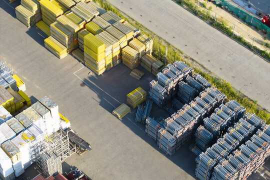Aerial view of stacked construction materials including yellow wooden beams and metal scaffolding frames in a storage yard in Krakow, Lesser Poland Voivode, Poland.