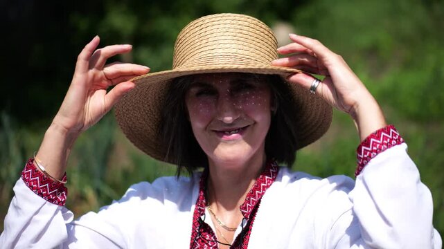 Portrait of happy ukrainian woman in traditional vyshyvanka at sunny summer day. Adult smiling lady wearing in straw hat looking into camera outdoor. Concept of national identity and patriotism