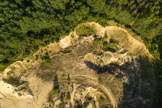 Aerial view of a sandy clearing with visible tire tracks bordering a dense pine forest in Rokiskis District Municipality, Panevezys County, Lithuania.