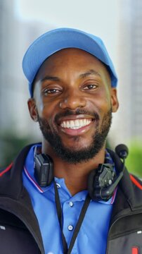 Portrait of a smiling delivery driver looking at the camera outdoors in an urban setting. Friendly courier representing modern logistics and delivery services. Vertical video