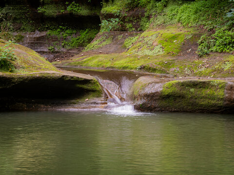 Scenic small waterfall cascading over mossy sandstone rocks into a tranquil pool in a lush green canyon