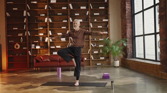Athletic mature man practicing tree pose at home, balance and wellness