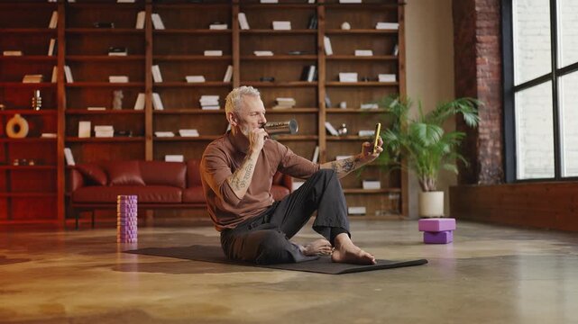 Stylish tattooed mature man recording a video message after a home workout