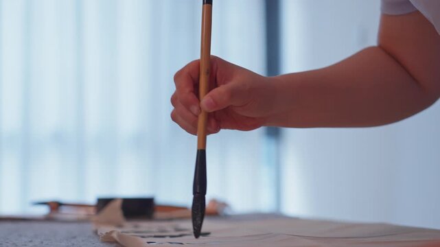 Figure in bright interior writes Chinese characters with brush after dipping in ink
