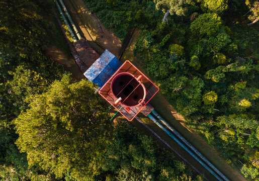 Aerial view of the Ketenger surge tank surrounded by dense tropical forest and industrial water pipelines in Baturaden, Central Java, Indonesia.