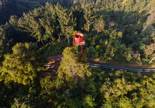 Aerial view of the Ketenger water tower structure surrounded by dense pine forest and lush greenery in Baturaden, Central Java, Indonesia.