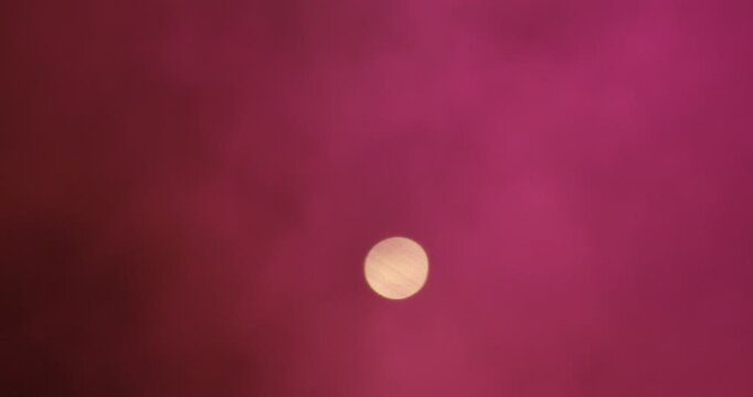 A dramatic view of the moon setting in the sky, partially veiled by thick red smoke
