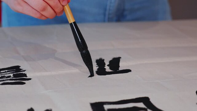 Close up front view of man holding a brush and writing on rice paper
