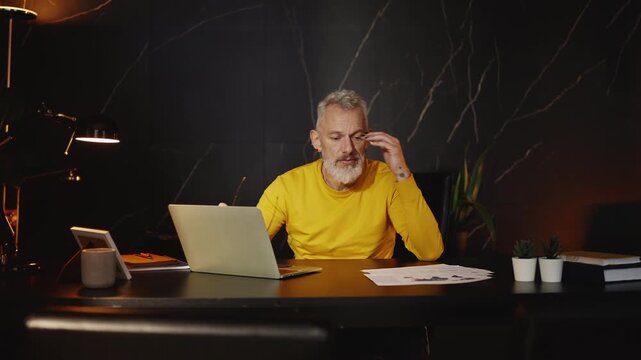 Overworked IT company boss taking off his glasses while working on a laptop