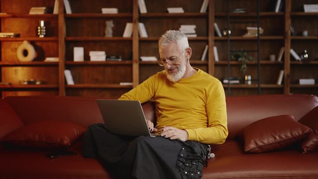 Happy mature man in stylish outfit shopping online on a laptop at home