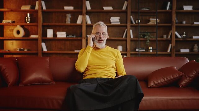 Mature man in trendy outfit arguing with a friend on the phone at home