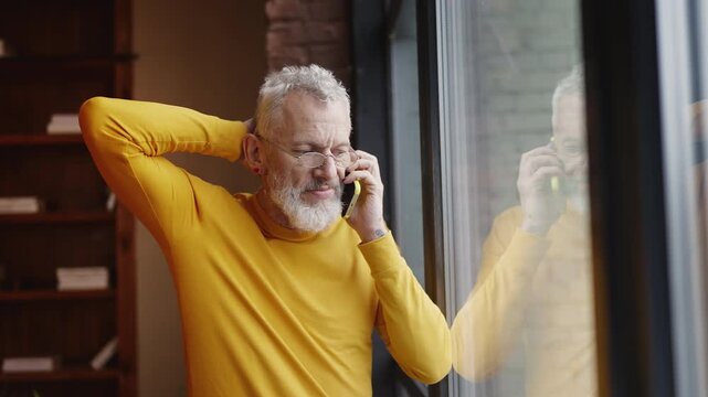 Stylish middle-aged man talking on a cellphone while looking out the window