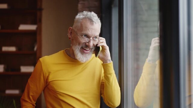 Cheerful man in his 50s talking with a friend on phone, celebrating good news