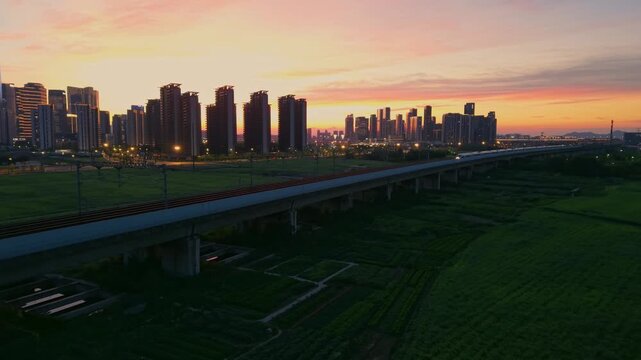 Aerial view of a high speed train travels on an elevated track past tall apartment buildings in a city suburb during sunset in China