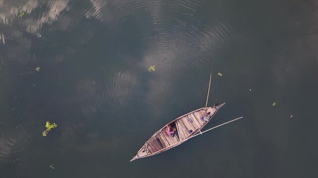 Aerial drone view of traditional wooden boat with two people navigating calm dark water serene