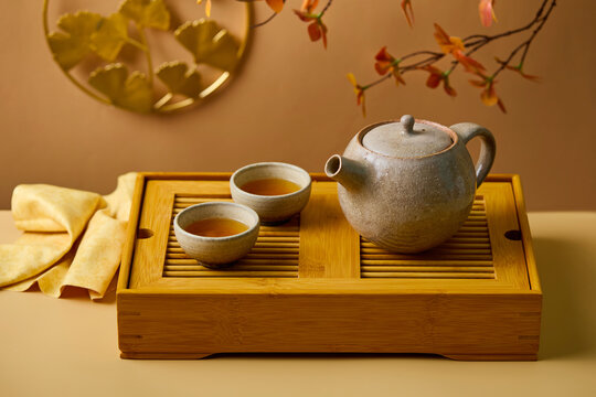 Asian tea ceremony set with ceramic teapot and golden ginkgo decor. Warm brown and beige background. Close up.