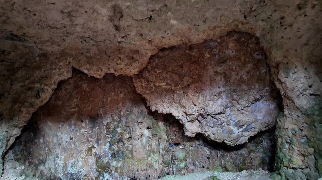 Xemxija, Malta 29.07.2026 - Heritage trail, Roman Baths, shelf like cut in the stone Dark cave walls show rough, textured surfaces. Greenish moss grows on damp, uneven stone. Light filters through nar