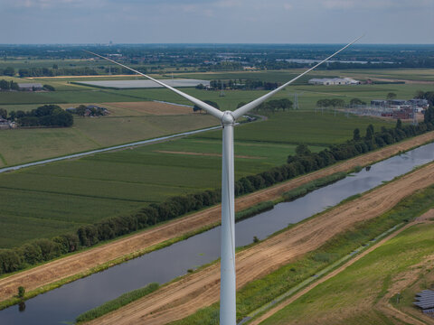 Aerial view of a wind turbine standing in a rural landscape with green fields and a canal in the Netherlands.